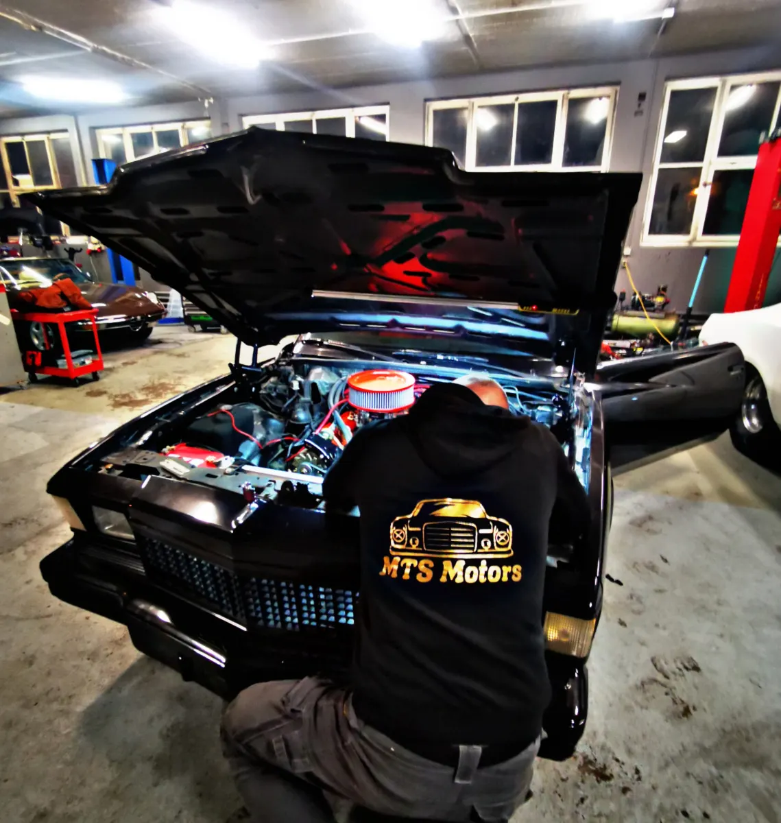 Mechaniker im MTS-Motors-Pullover arbeitet unter der offenen Motorhaube