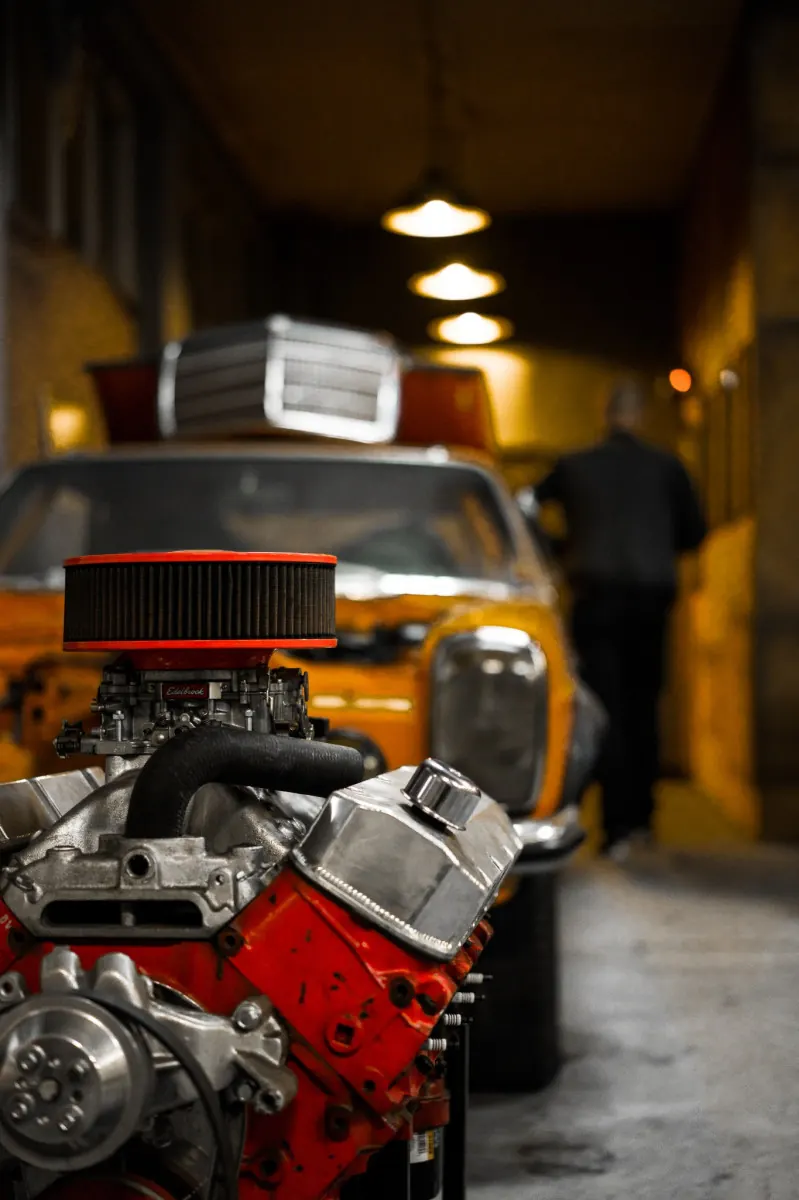 V8-Motor mit rotem Luftfilter, dahinter die Werkstatthalle