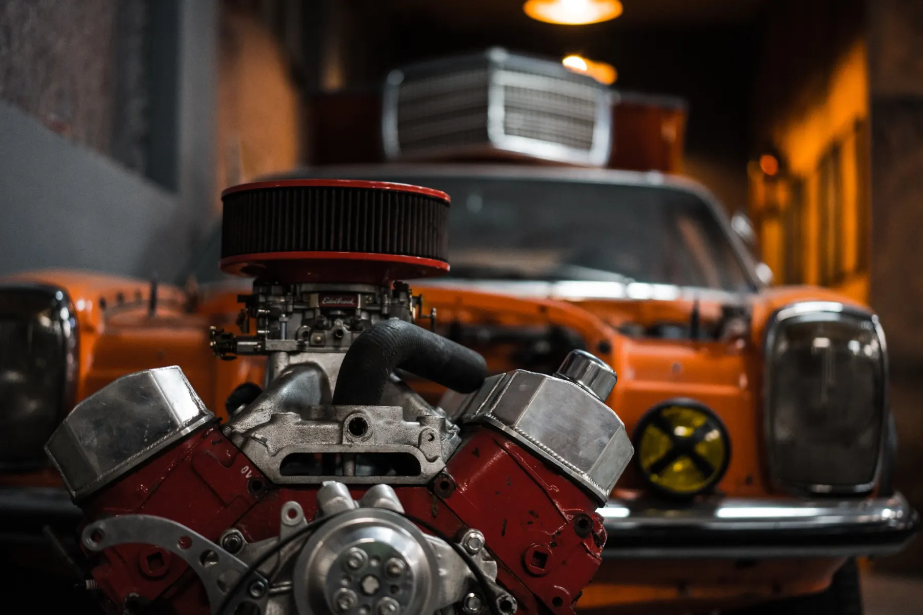 Offener V8-Motor vor einem orangen Oldtimer